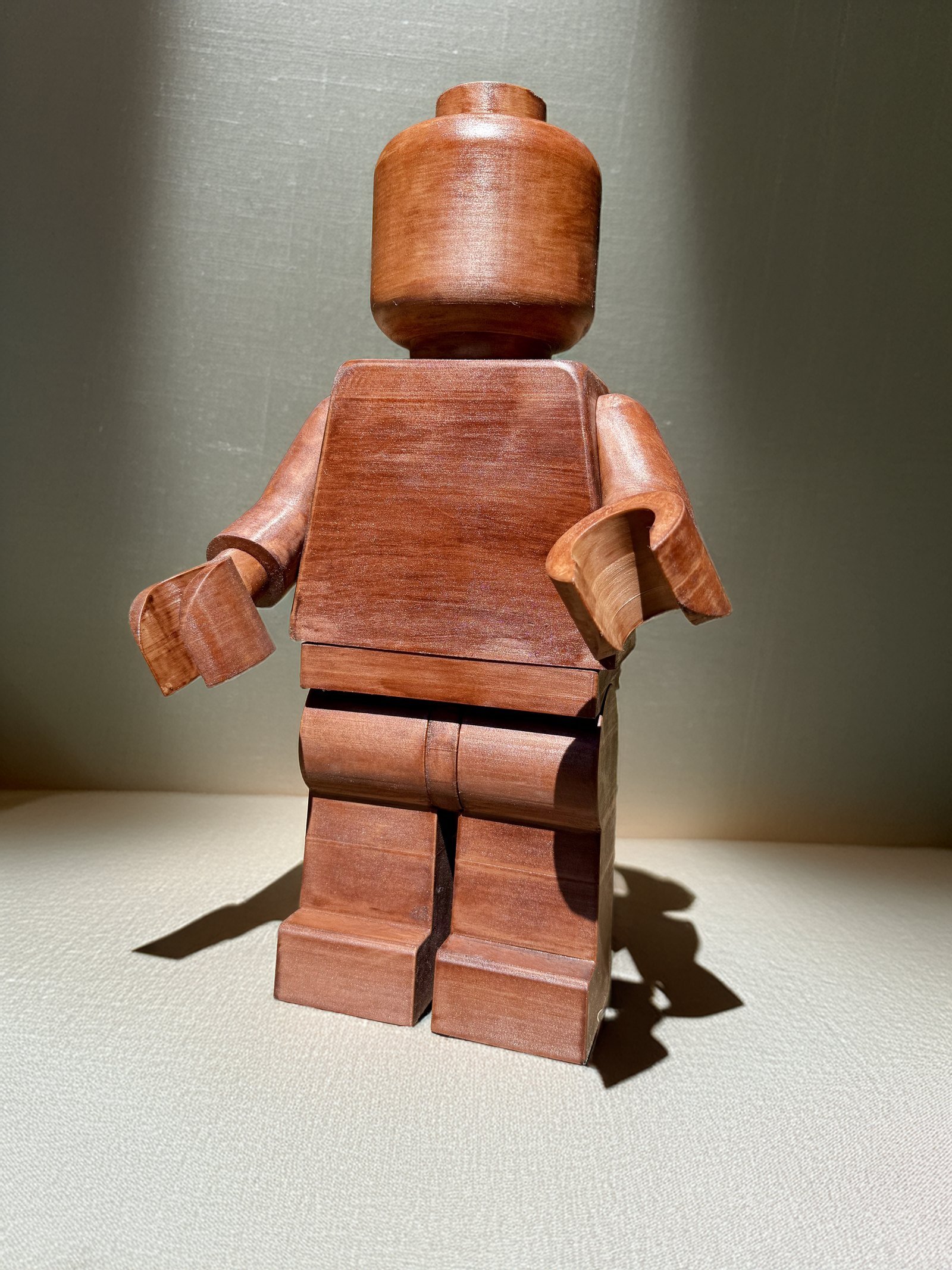The Wood Edition Mega Figure in stained wood, lit from the side so the grain runs through the torso and legs