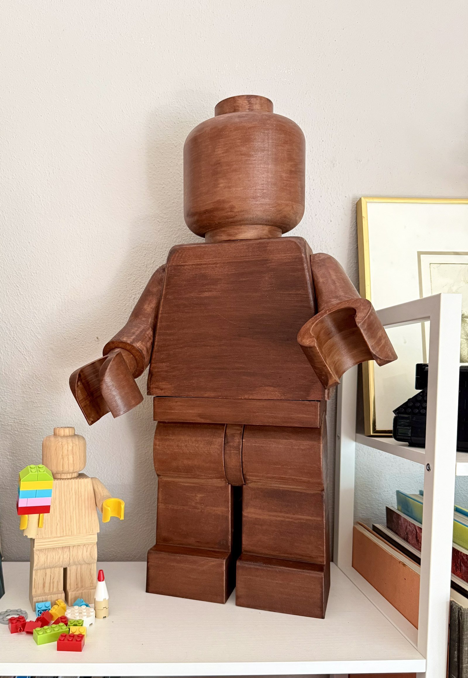 The Wood Edition on a shelf beside a smaller unstained wood figure, showing the difference the American Walnut stain makes